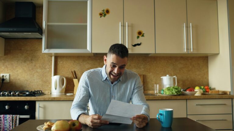 A person reviews suspicious account statements, identity documents, and a laptop at a kitchen table.